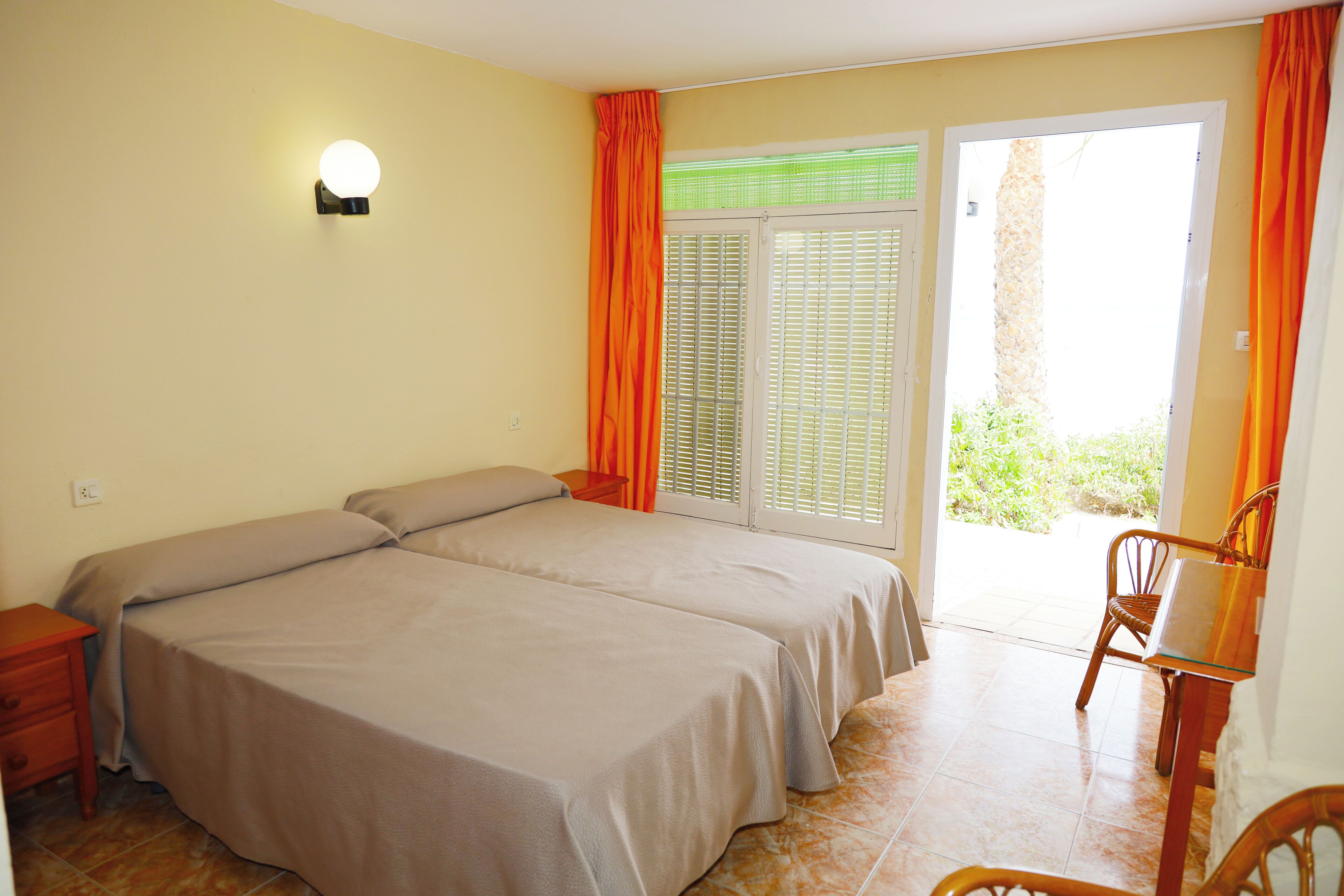 A bedroom with two beds, a nightstand, a chair, and a sliding glass door leading to a balcony.