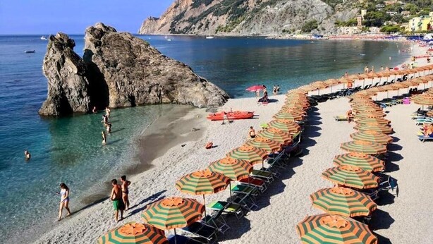 A beach with rows of umbrellas and sun loungers, rocky formations, and a clear view of the sea. - Affittacamere Alle 5 Terre (Monterosso al Mare)