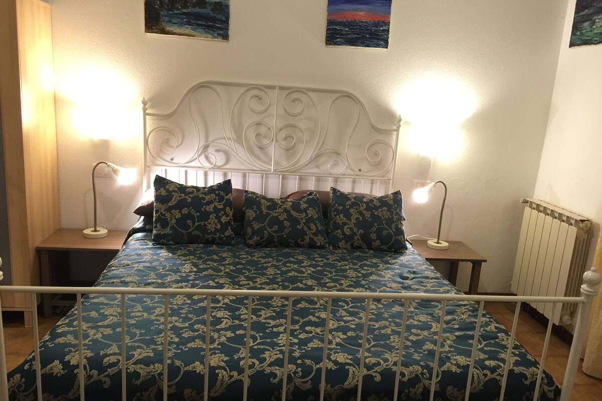 A bed with a white metal frame and a blue floral bedspread. There are two bedside tables with lamps.