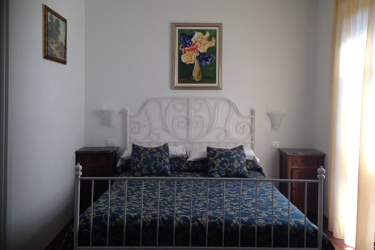 A bedroom with a white metal bed frame, a blue patterned bedspread, and two bedside tables.