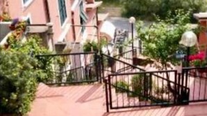 A row of pink buildings with balconies, surrounded by greenery and a paved walkway. - Affittacamere Alle 5 Terre (Monterosso al Mare)