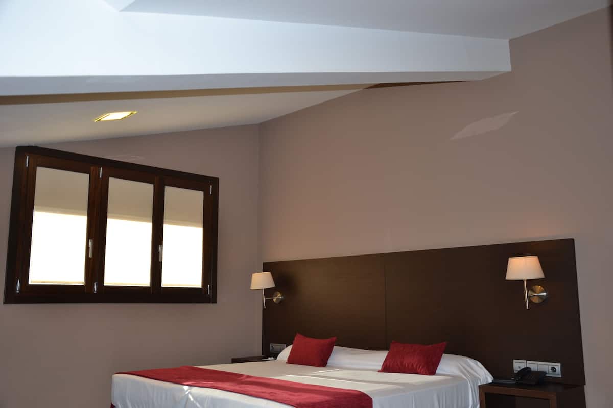 A hotel room with a large bed, two bedside lamps, a nightstand, and a window with a wooden frame.