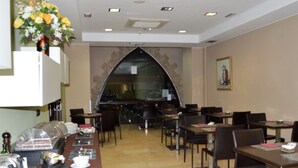 A restaurant with a long counter, dining tables, and chairs. There is a flower arrangement on the wall and a painting on the wall. - Hotel Vilassar (Vilassar de Mar)