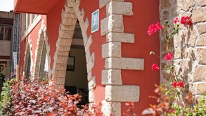 A hotel entrance with a stone facade, a sign with a 'H', and red flowers in the foreground. - Hotel Vilassar (Vilassar de Mar)