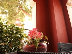 A table with a vase of pink flowers, a potted plant, and a red curtain in the background. - Hotel Vilassar (Vilassar de Mar)