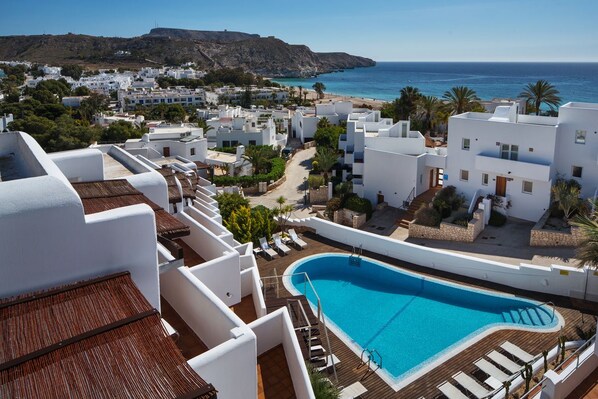 A resort with a swimming pool, white buildings, and a view of the sea.