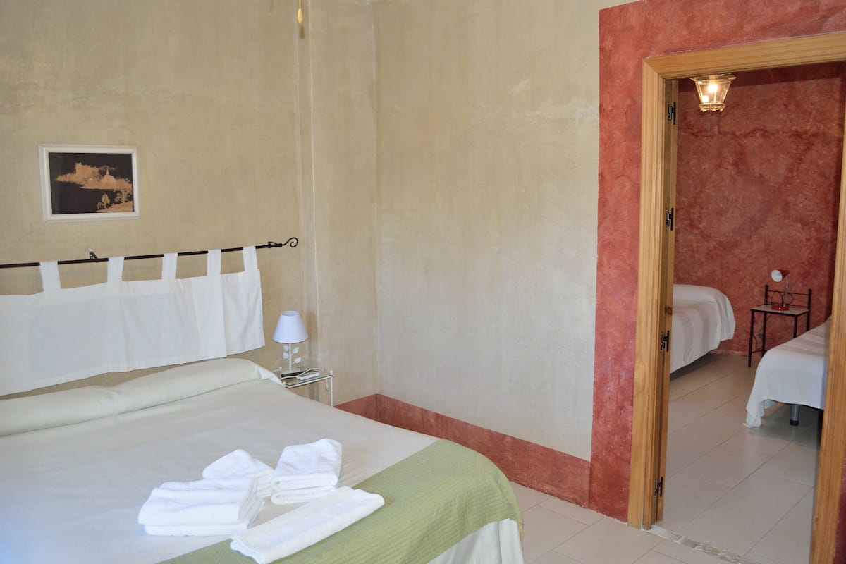 A hotel room with a bed, a bedside table with a lamp, a framed picture on the wall, and a mirror reflecting another bed.