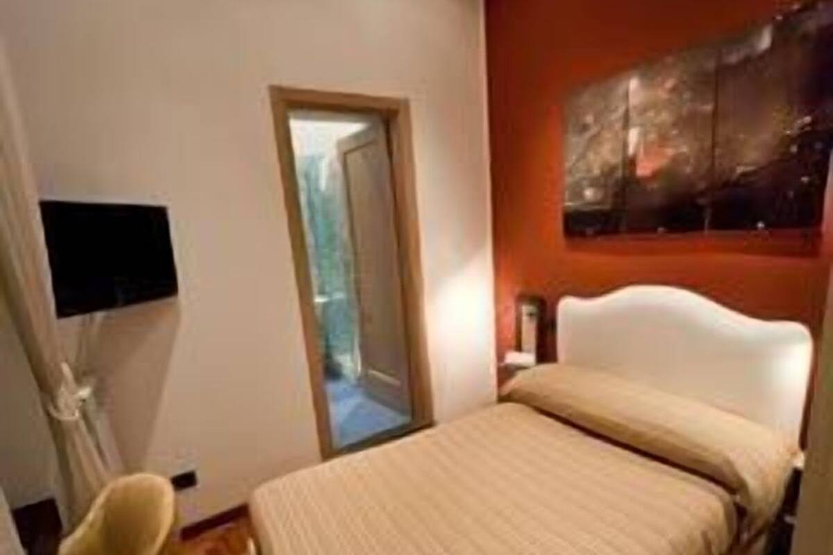 A bedroom with a bed, a chair, a TV, and a painting on the wall.