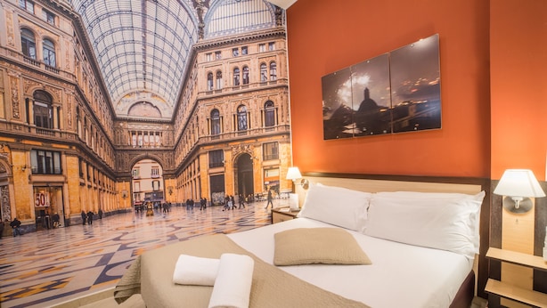 Habitación de hotel con una cama grande, dos lámparas de noche y vista al interior de un edificio histórico.