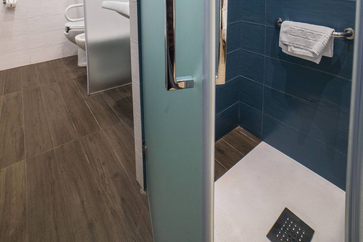 A modern bathroom with a glass shower enclosure, a white toilet, and a blue-tiled shower wall.