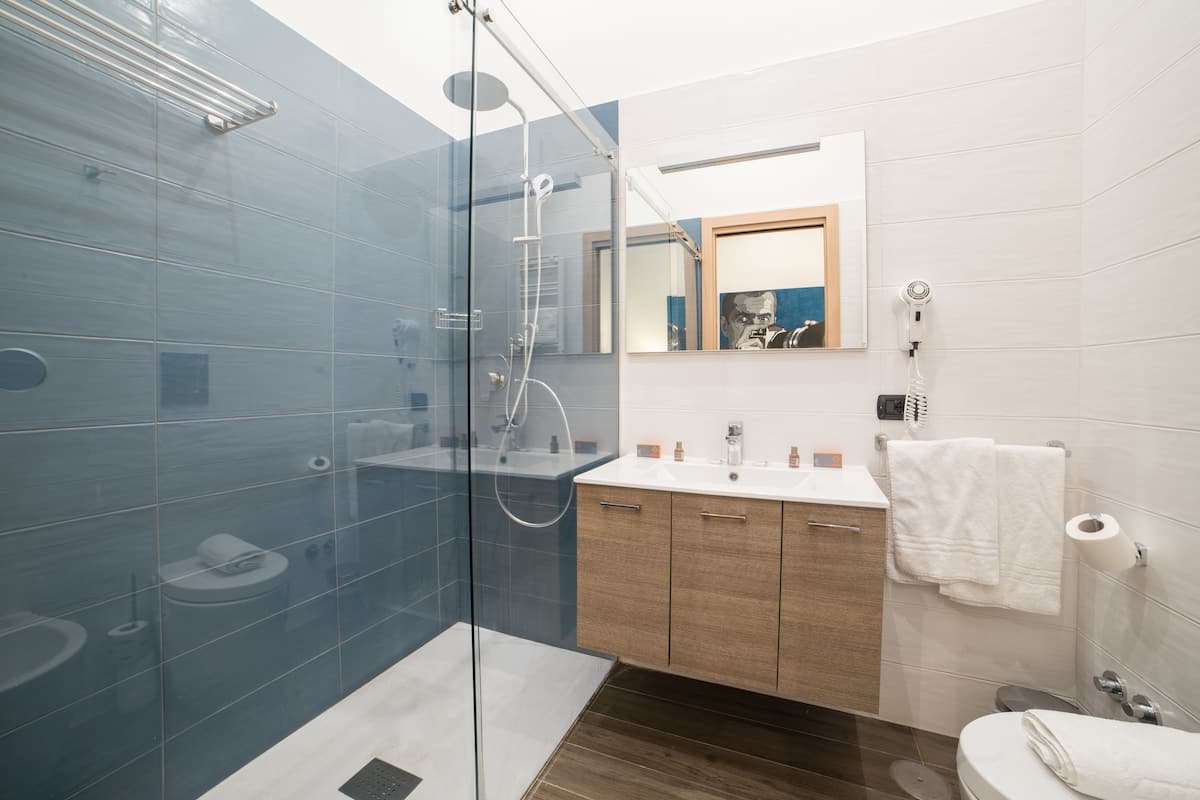 A modern bathroom with a glass-enclosed shower, wooden cabinets, a white sink, and a mirror with a framed artwork.