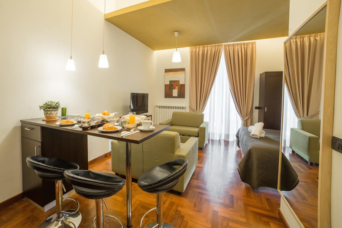 A hotel room with a dining area, a sofa, a TV, and a mirror.