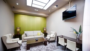 A modern living room with a green accent wall, a flat-screen TV, a sofa, two armchairs, a coffee table, and a dining area with chairs and a table. - San Pedro (Langreo)