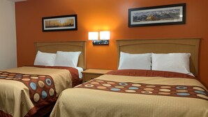 Habitación de hotel con dos camas, cada una con una colcha estampada y almohadas blancas. Se observan dos cuadros en la pared, una mesita de noche con una lámpara y un cabecero de madera.