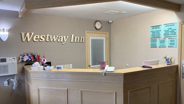 Mostrador de recepción en Westway Inn con un reloj, banderas y carteles informativos.