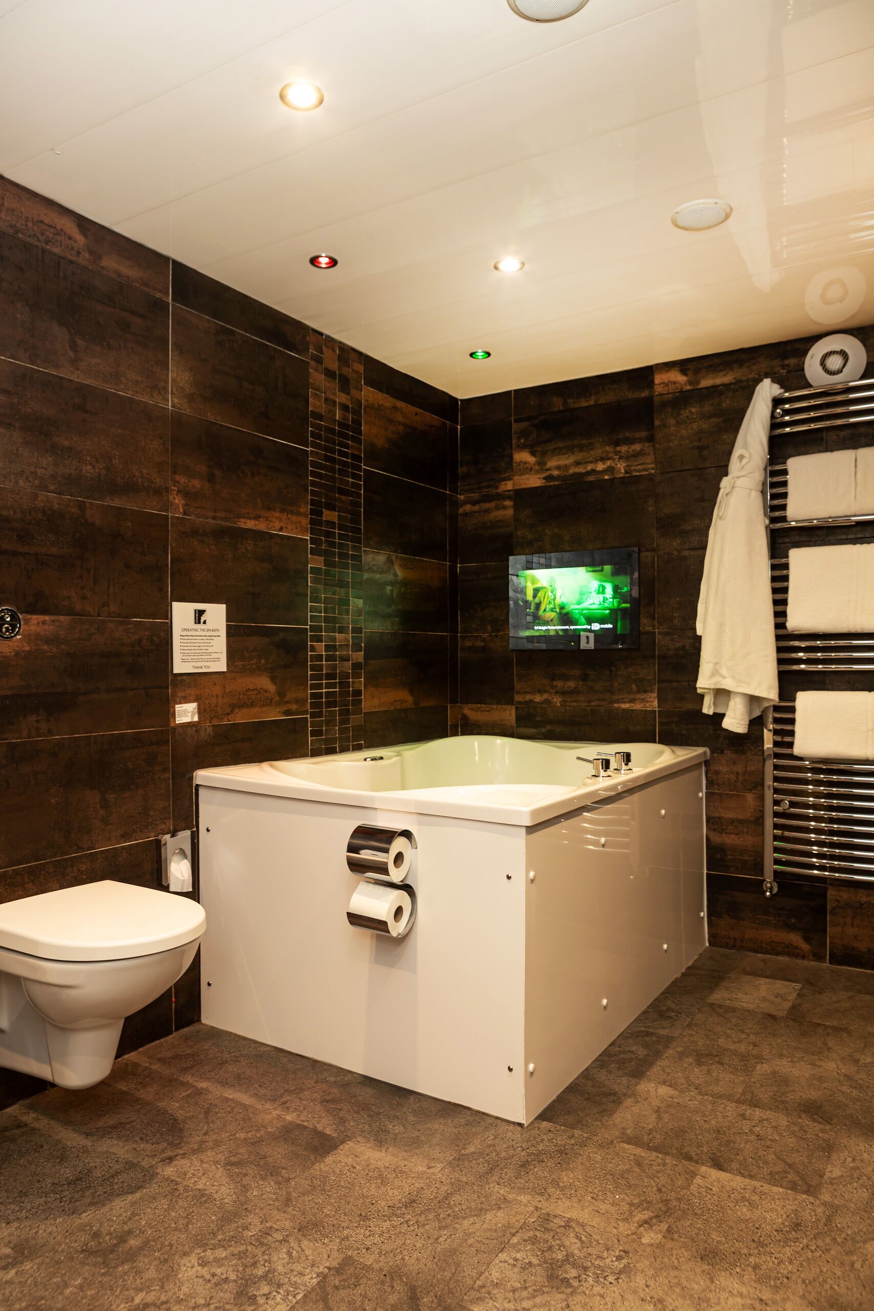 A modern bathroom with a large bathtub, a toilet, and a wall-mounted TV.