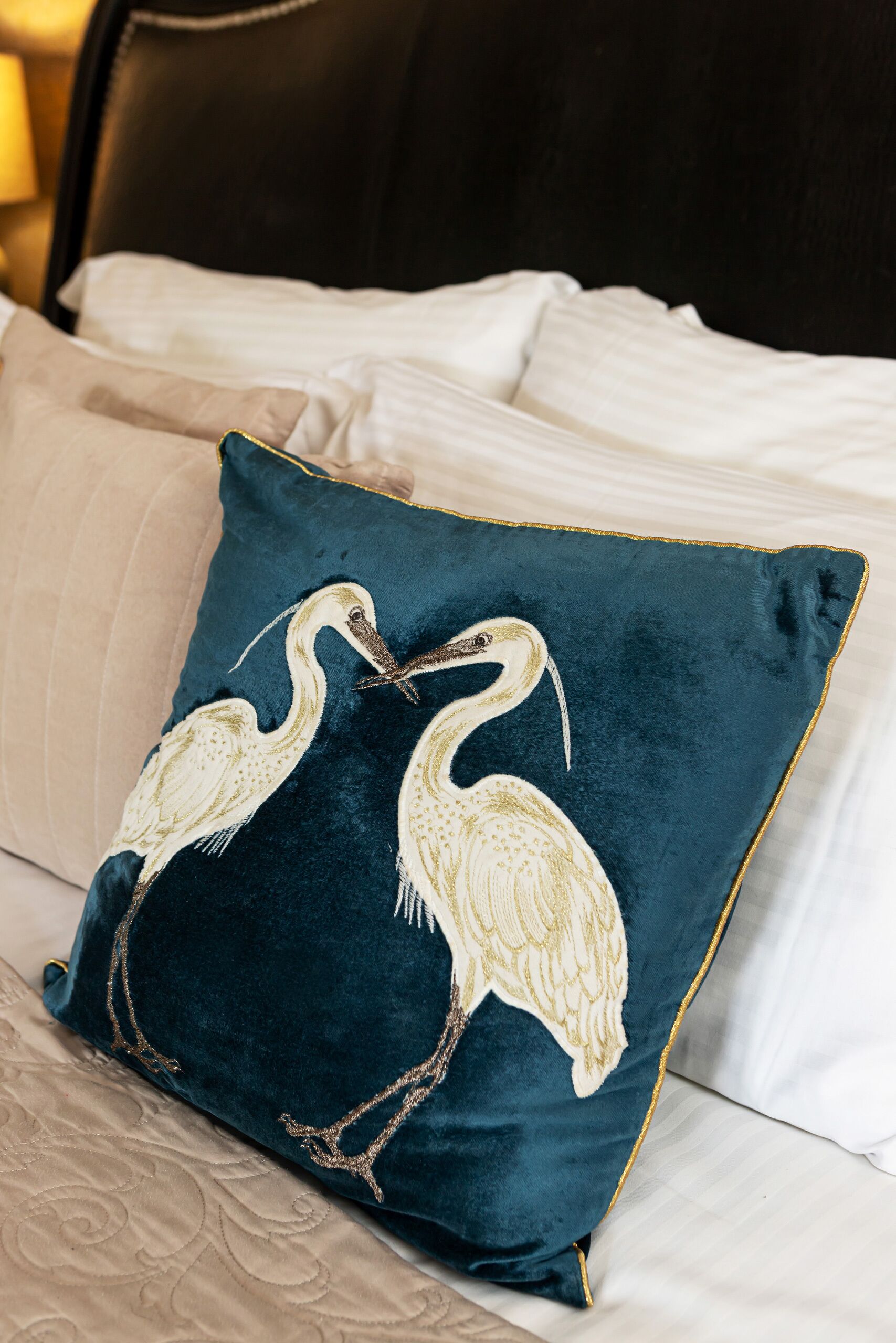 A bed with white linens and a dark blue pillow with a bird design.