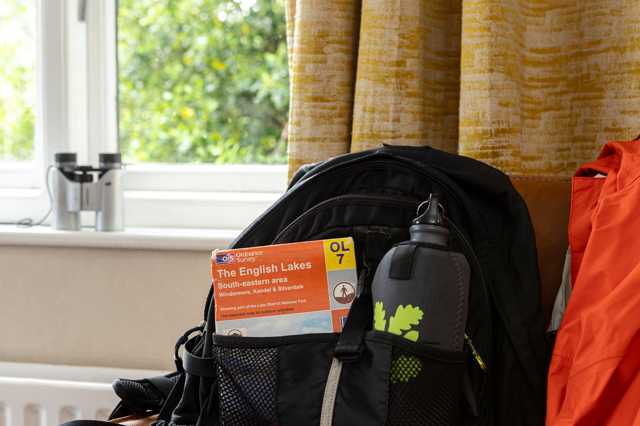 A window with curtains, a radiator, and a map of The English Lakes South-eastern area in a bag.