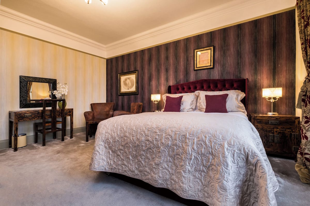 A spacious bedroom with a large bed, a wooden desk, and a chair.