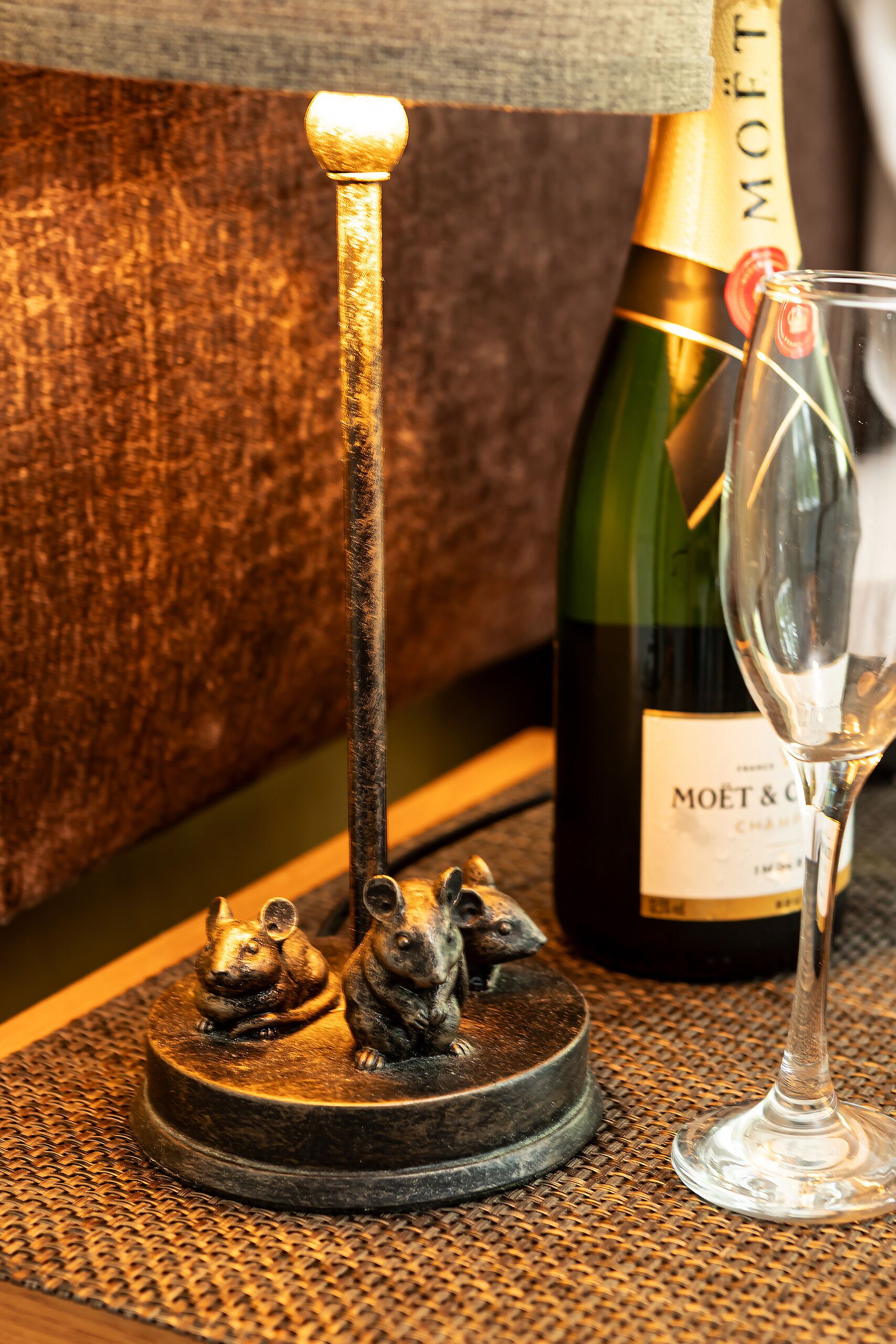 Una botella de Moët & Chandon, una copa y una escultura metálica de dos ratones sobre una estera tejida.