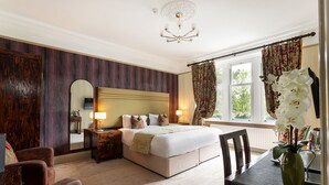 A bedroom with a large bed, a dresser, a mirror, a chandelier, and a window with curtains. - Howbeck Guest House (Windermere)