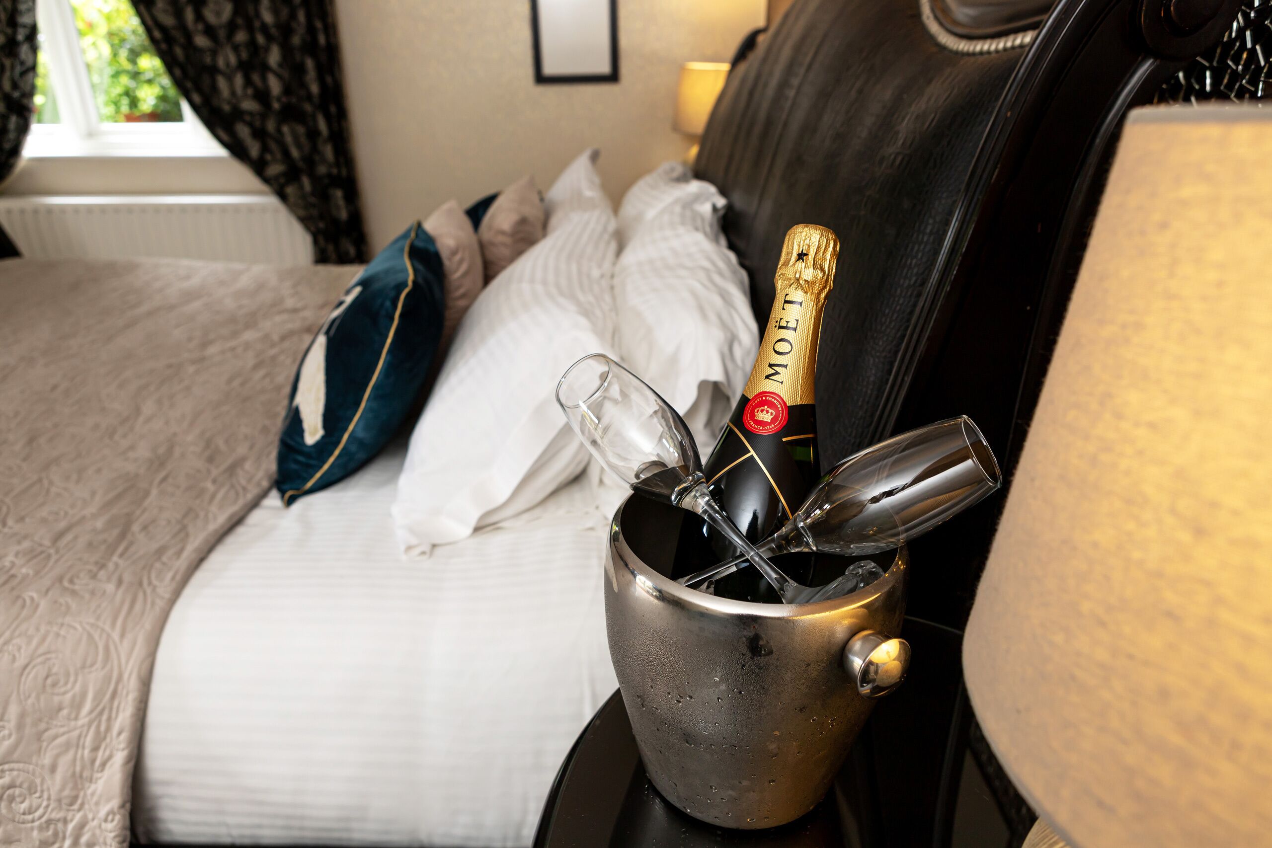 A bed with a champagne bottle and glasses in a metal container.