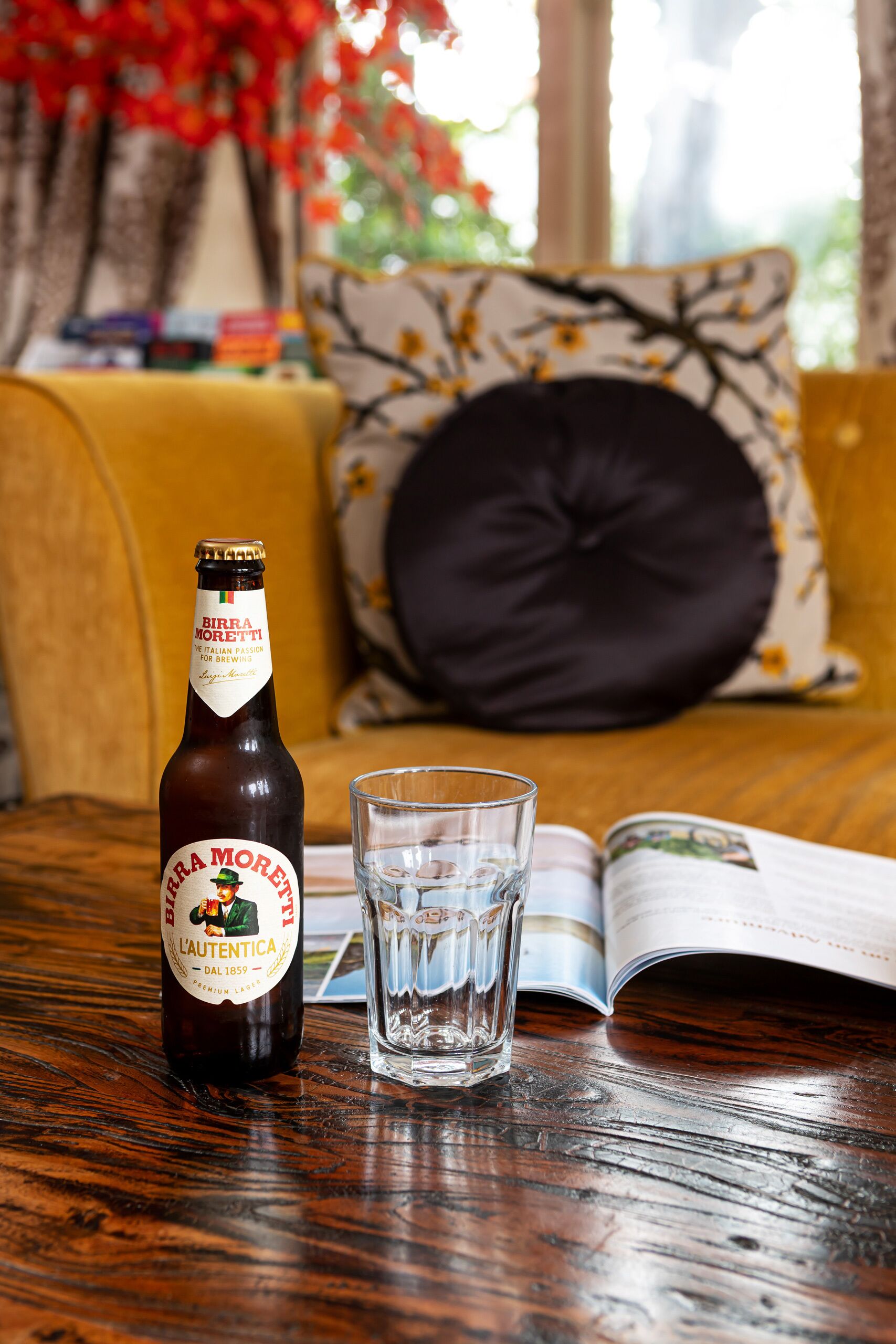 Una botella de cerveza Birra Moretti, un vaso y una revista sobre una mesa de madera.