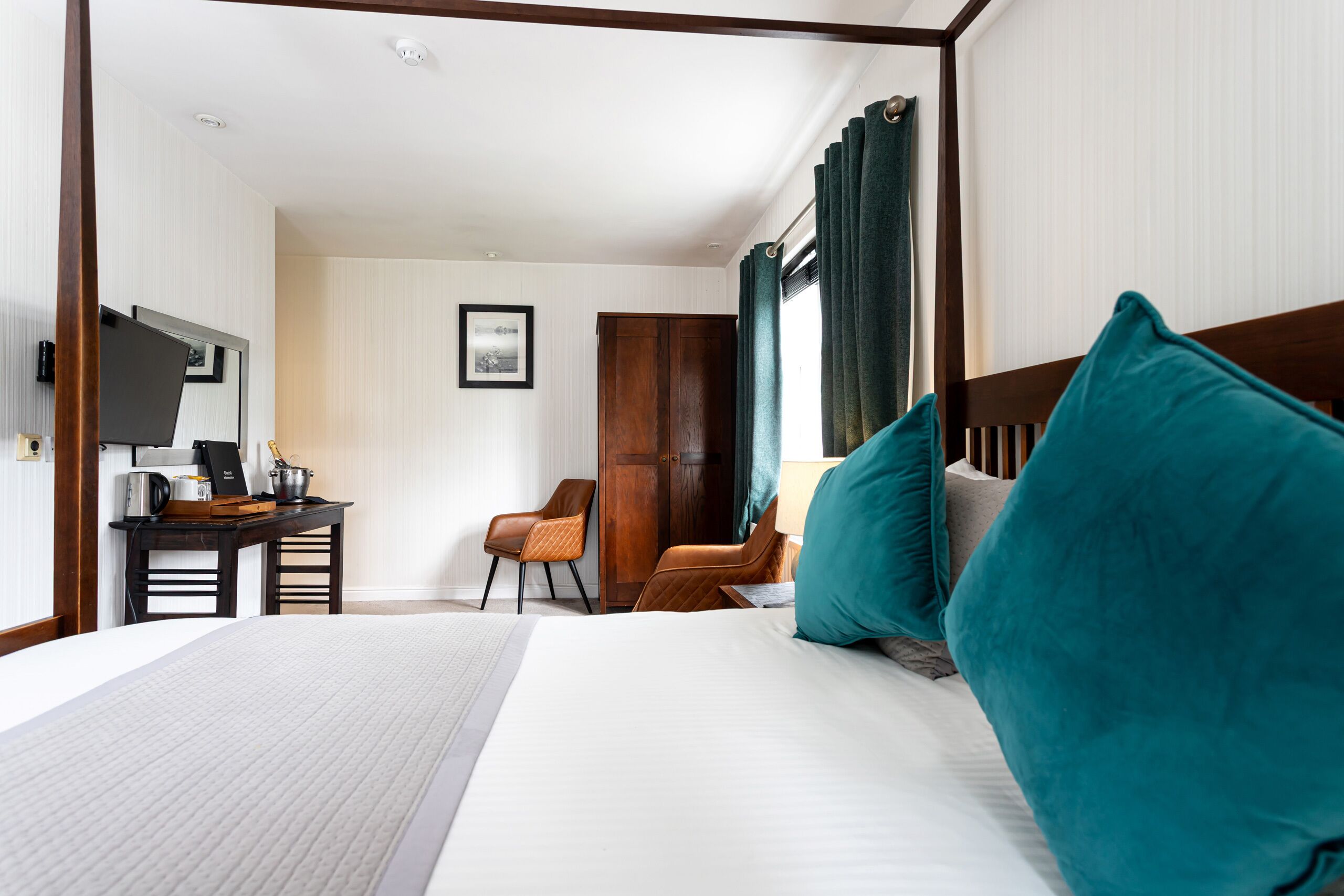 A hotel room with a large bed, two chairs, a desk with a computer, and a television.