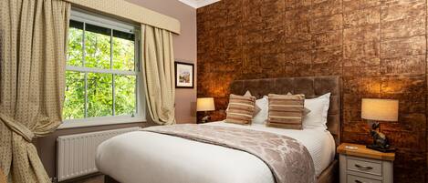 Un dormitorio con una cama grande, una mesita de noche con lámpara, una ventana con cortinas y una pared de ladrillo.
