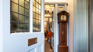 A hallway with a wooden door, a large clock, and a patterned floor. - Howbeck Guest House (Windermere)