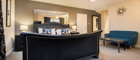 A bedroom with a large bed, a blue sofa, a small table, and a mirror on the wall.