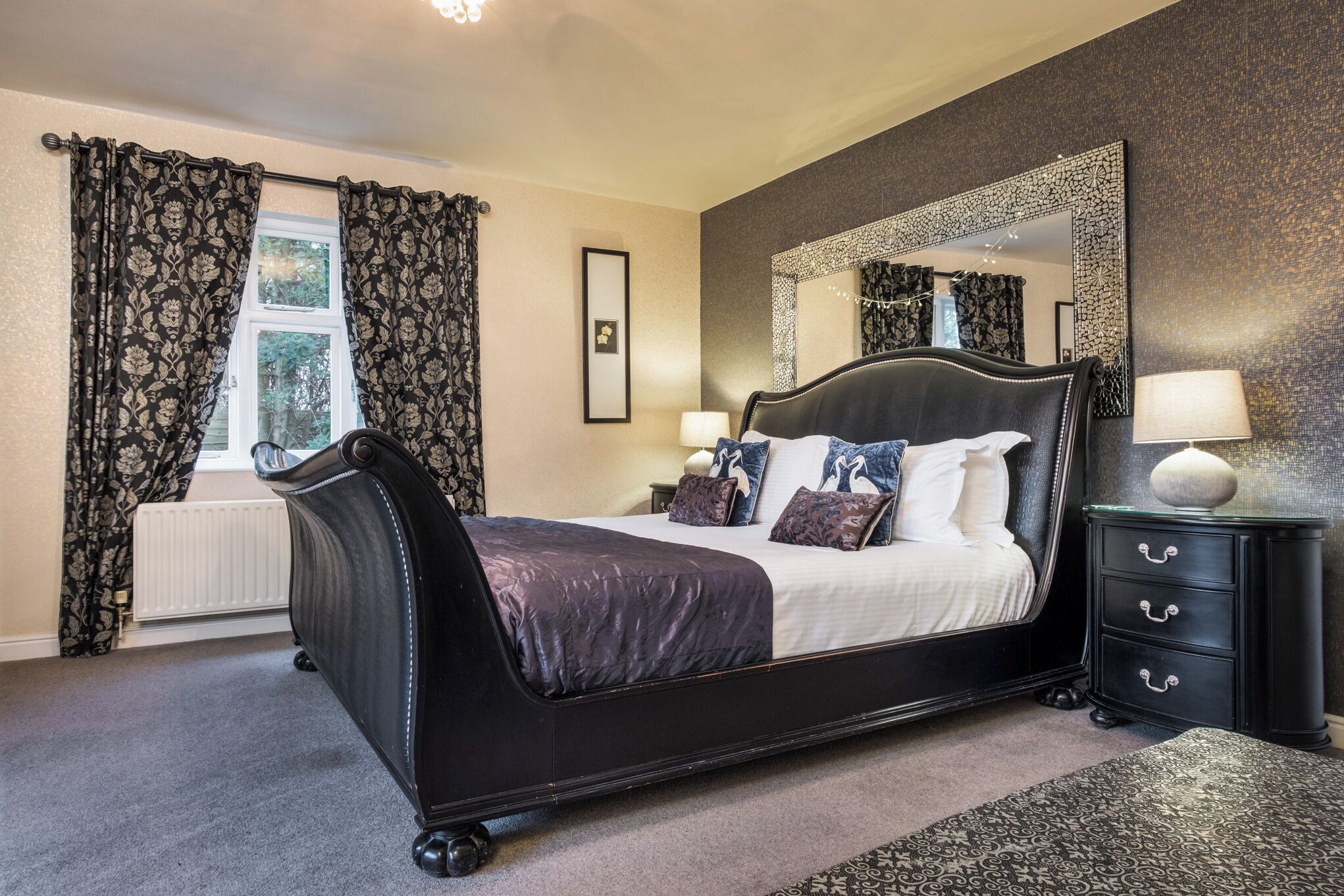 A bedroom with a large bed, a dresser with drawers, a mirror, and a window with curtains.