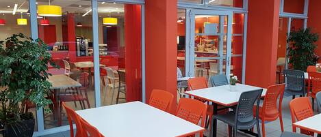 A modern restaurant with red and white color scheme, glass partitions, and indoor seating with orange chairs.