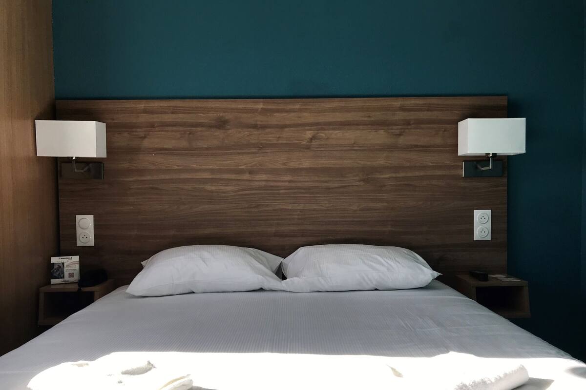 Una cama bien hecha con sábanas y almohadas blancas, dos lámparas de noche y un cabecero de madera.