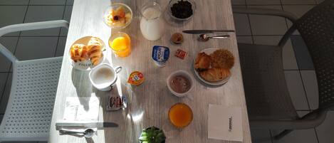 Et morgenbord med croissanter, frugt, juice, mælk og en lille plante.