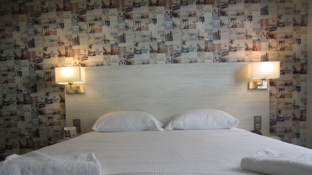 A hotel room with a neatly made bed, two wall-mounted lamps, and a wall decorated with a collage of images. - The Originals Access, Hôtel les Iris (Berck-sur-Mer)