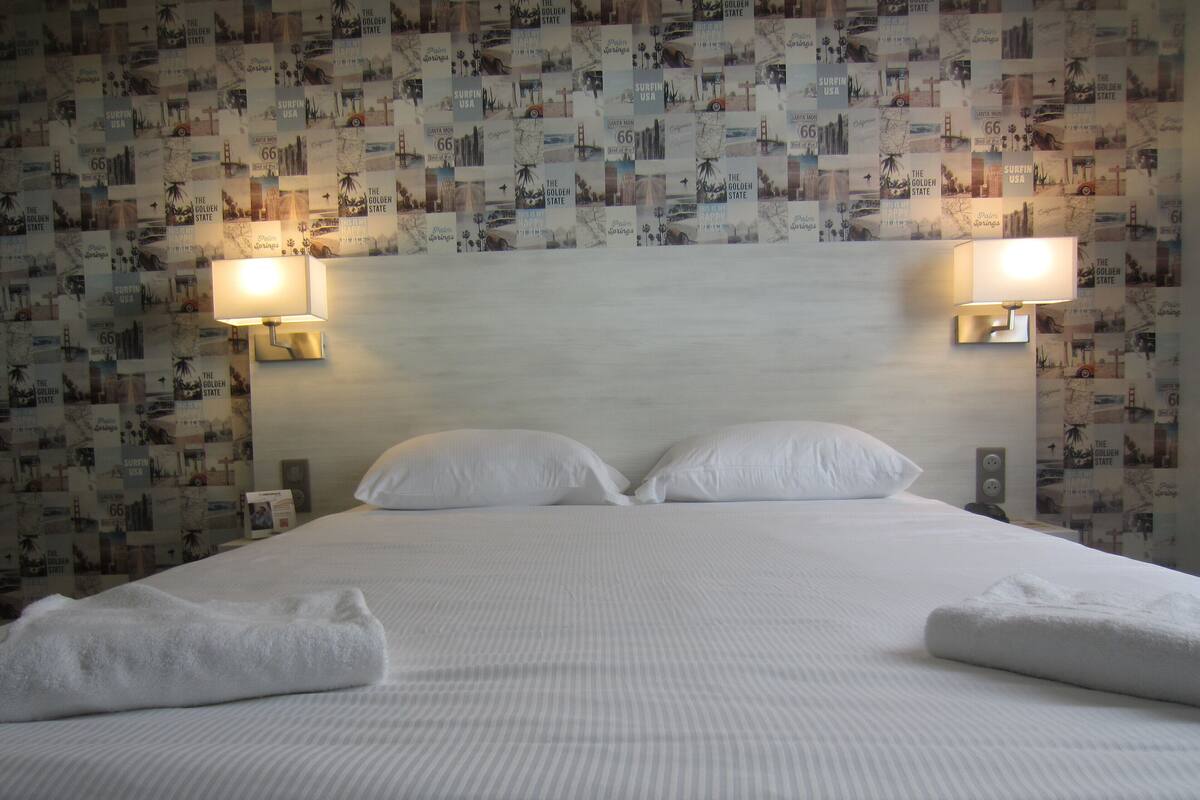 Una habitación de hotel con una cama bien hecha, dos lámparas fijadas a la pared y una pared decorada con un collage de imágenes.