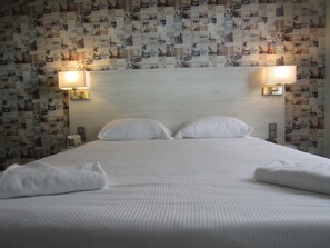 Una habitación de hotel con una cama bien hecha, dos lámparas fijadas a la pared y una pared decorada con un collage de imágenes.