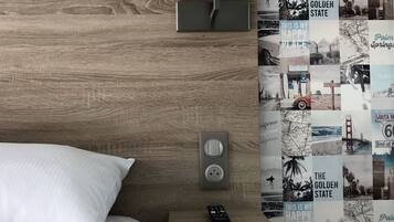 Hotelkamer met een houten hoofdbord, een wit bed met een kussen, een nachtkastje met een afstandsbediening, en een muur versierd met foto's met een retro Palm Springs en Californië thema.