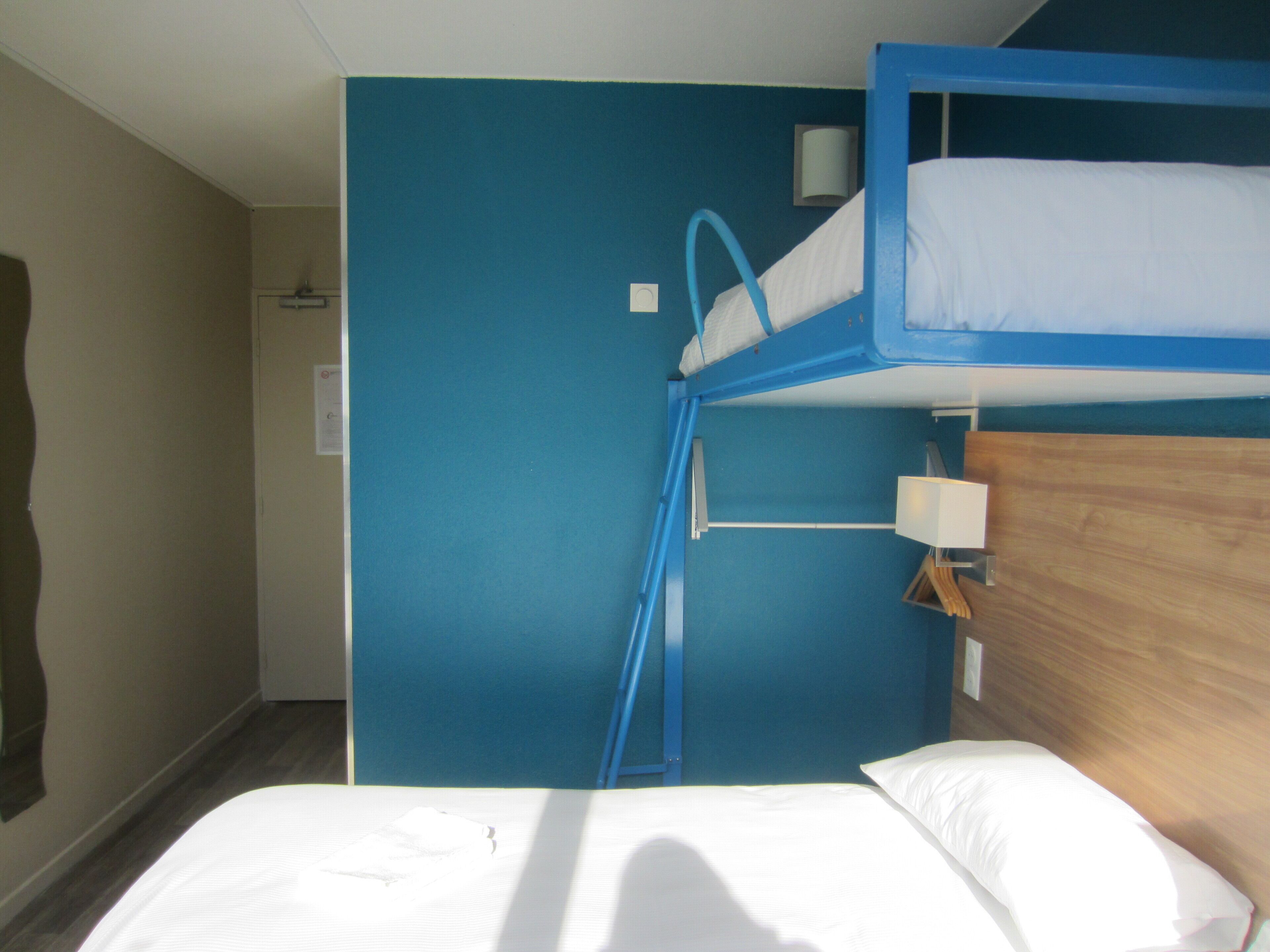 Ein Schlafzimmer mit Etagenbett, blauer Wand, Holz-Kopfteil und weißem Bett.