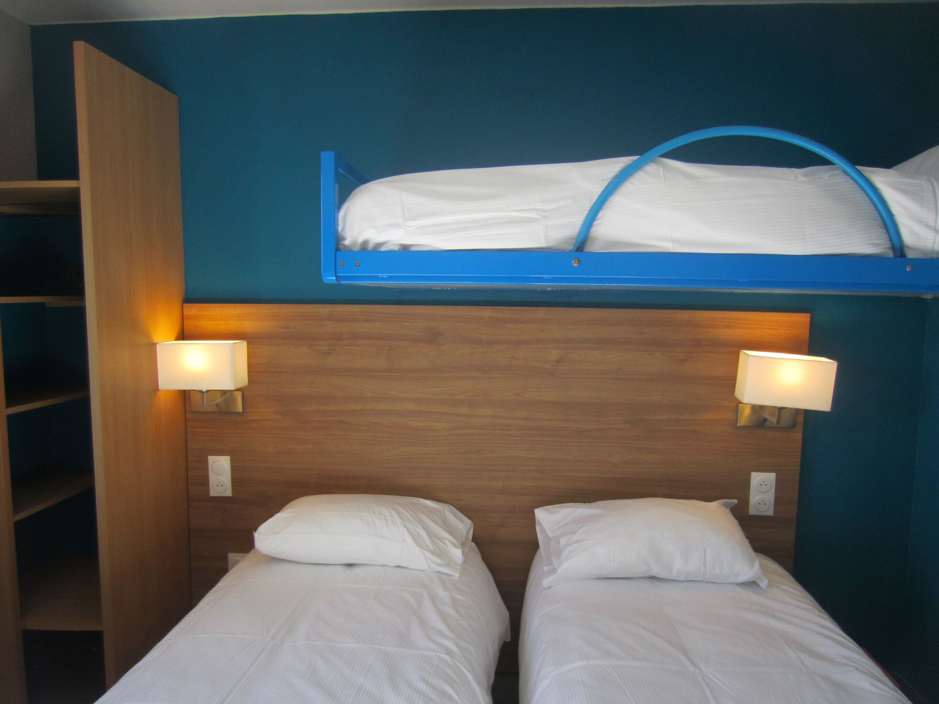 Una habitación con dos camas individuales y una litera, paredes de madera y lámparas fijadas a la pared.