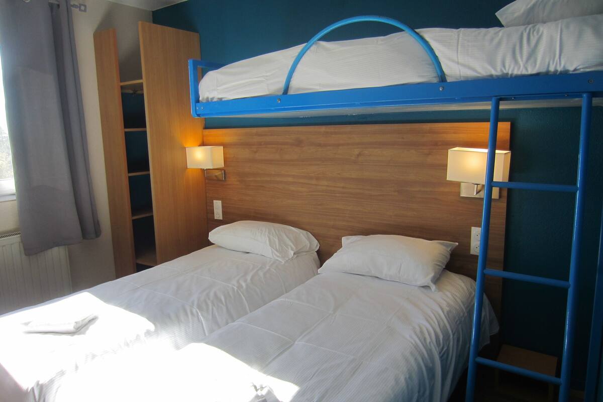 Una cama litera con dos camas blancas, cabecero de madera y dos lámparas fijadas a la pared.
