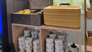 A kitchen area with a microwave, a coffee machine, and a stack of yellow plates on a shelf. - The Originals Access, Hôtel les Iris (Berck-sur-Mer)