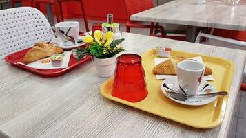 A dining table with trays of food, including croissants, a red glass vase, and a potted plant.