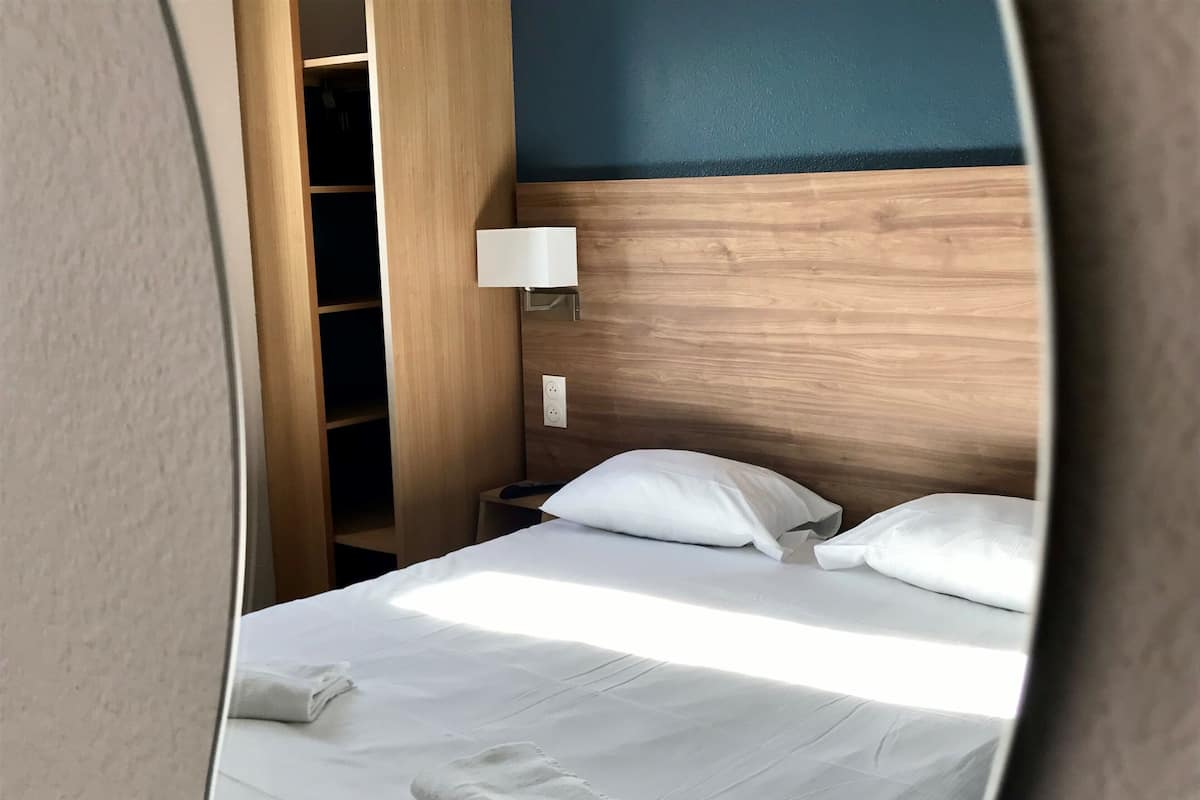 Una habitación de hotel con una cama bien hecha, una lámpara de noche y un cabecero de madera.