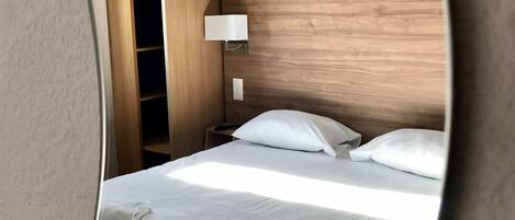 A hotel room with a neatly made bed, a bedside lamp, and a wooden headboard.