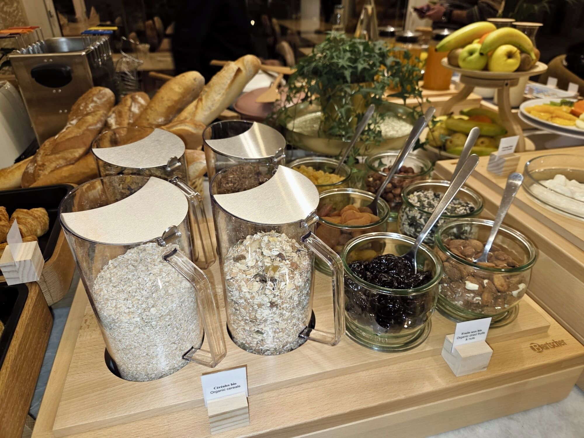 A buffet with various food items including bread, fruits, and cereals.