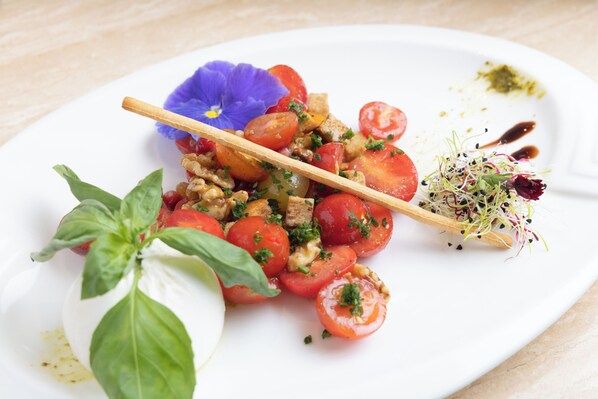A plate of food with tomatoes, basil, and a blue flower.