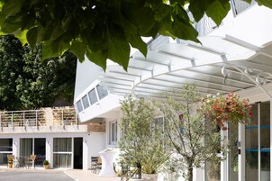 Un edificio moderno con un área exterior cubierta, plantas en macetas y mesas al aire libre.