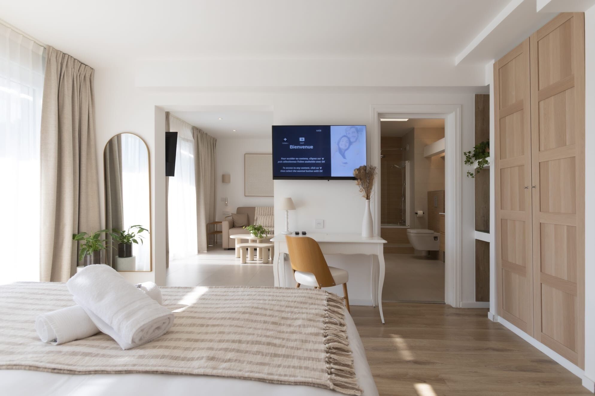 Een moderne hotelkamer met een bed, een bureau en een televisie waarop een welkomstboodschap staat.